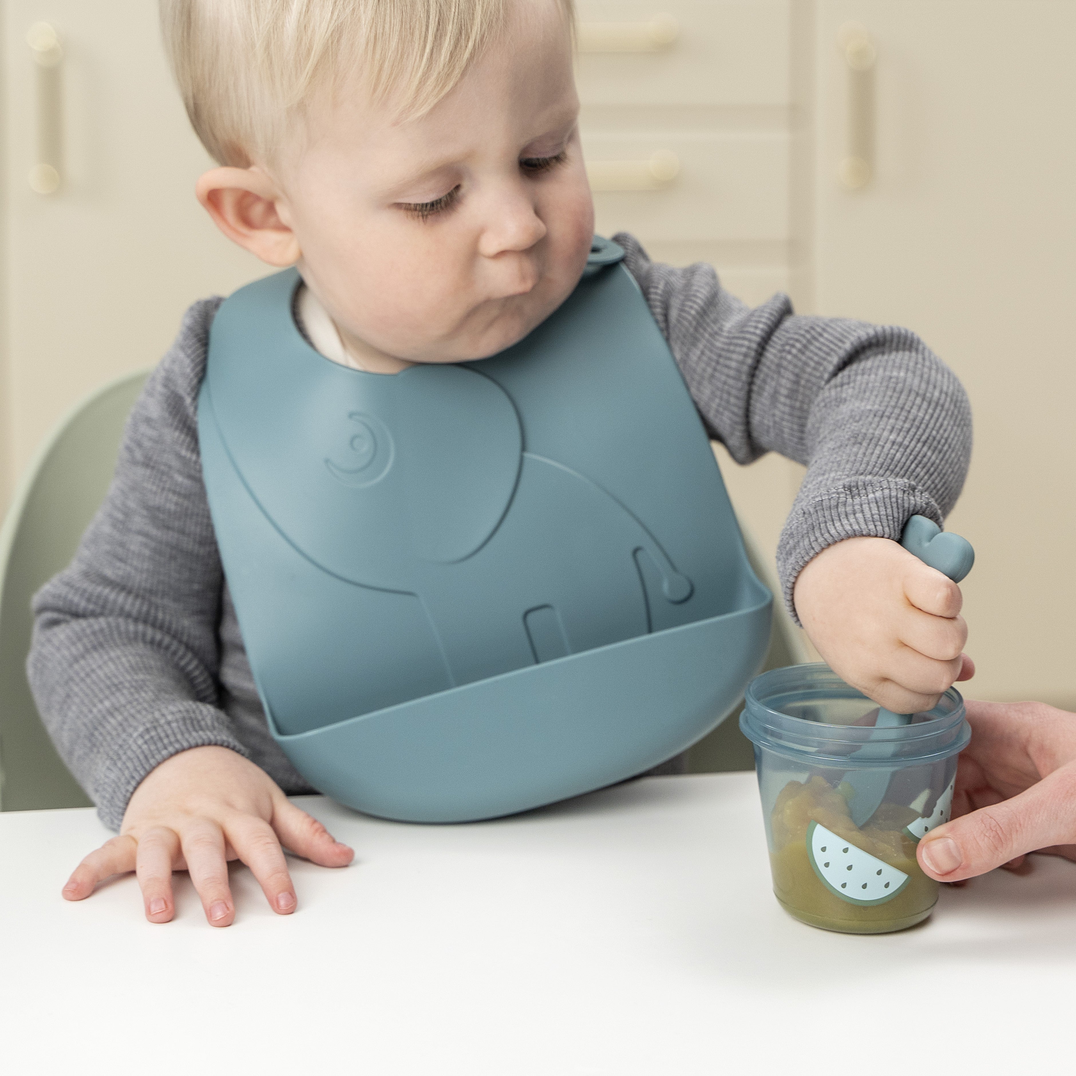 Child using Done by Deer cutlery to scoop food from a Done by Deer baby food container