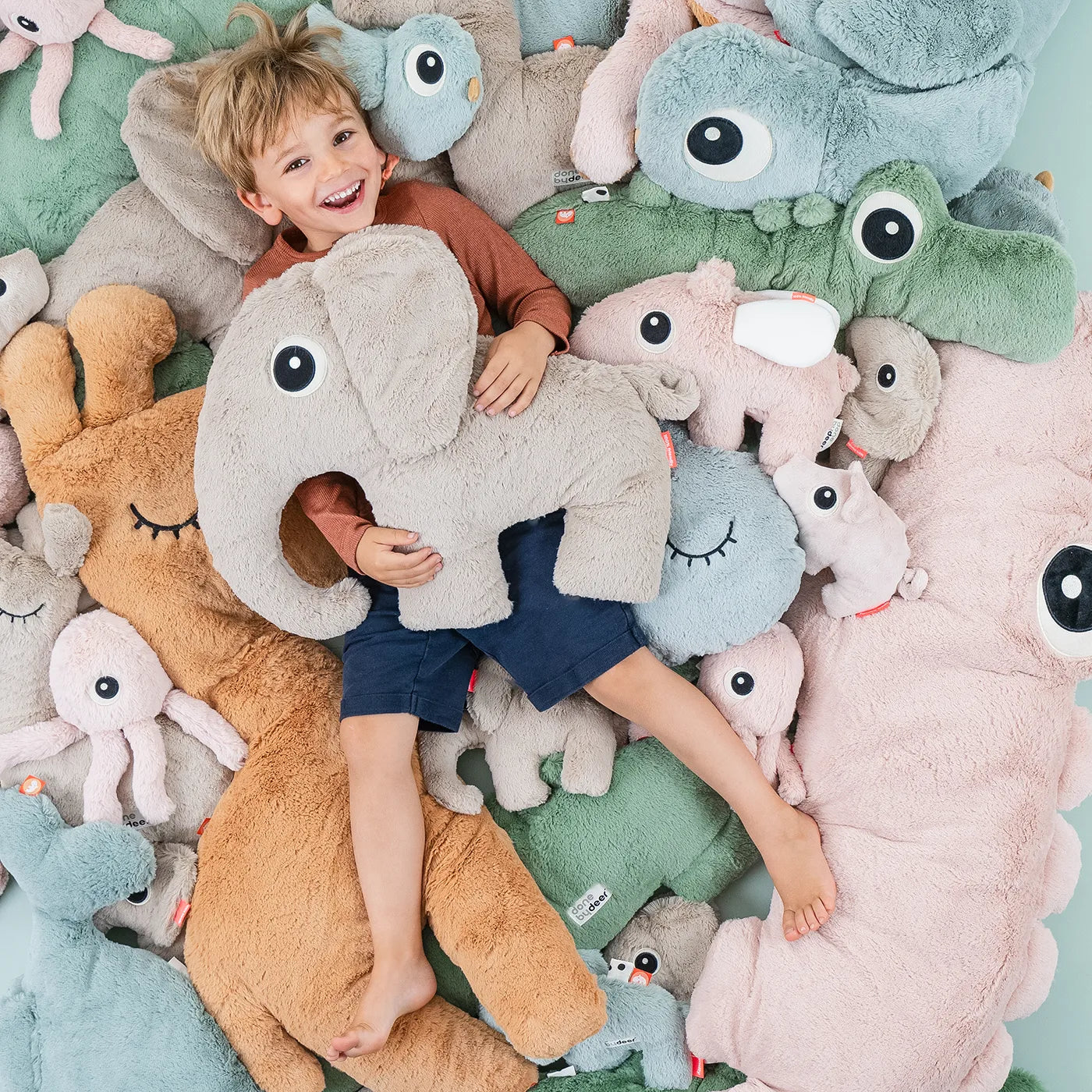 Boy lying among alle the Deer friends cuddle toys