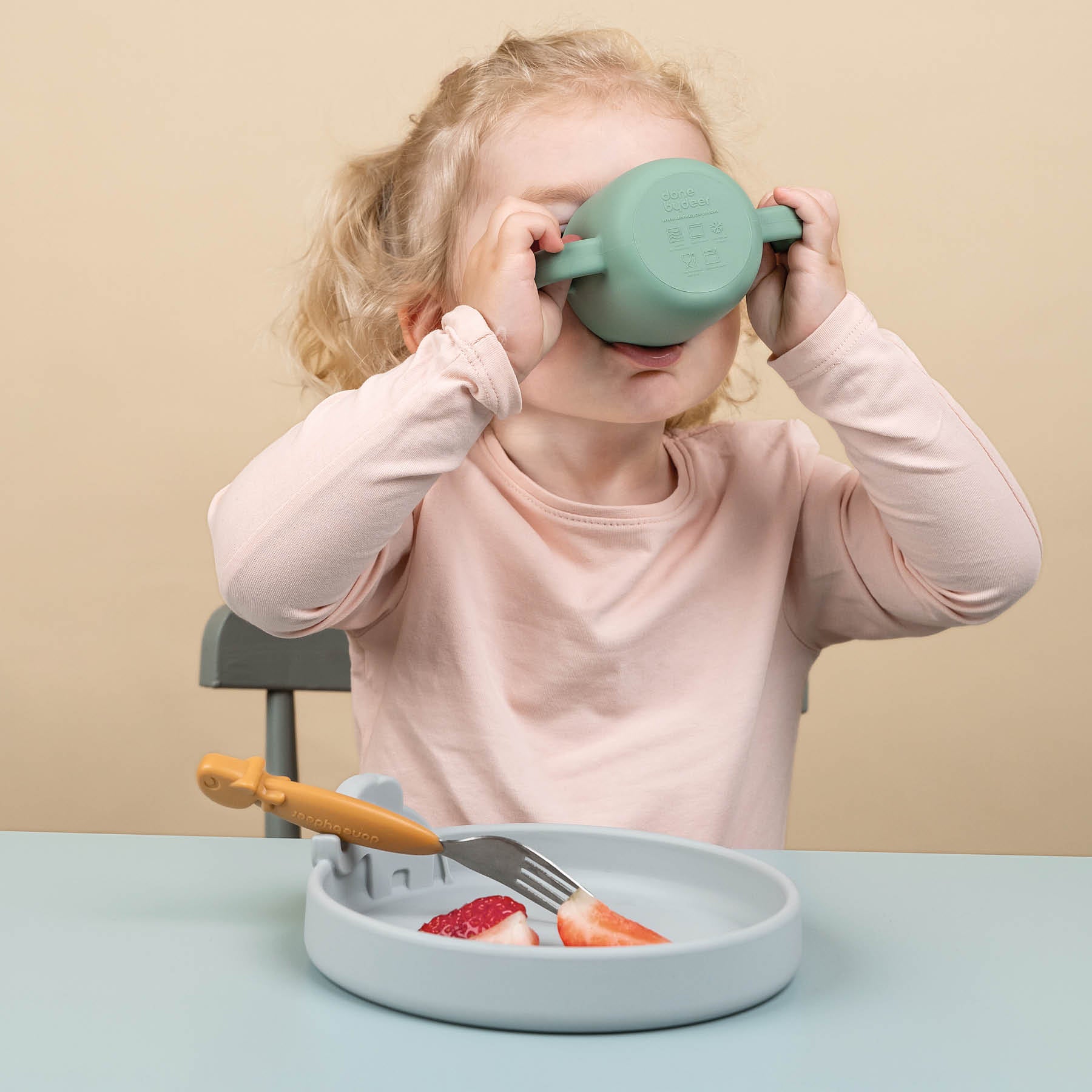 Girl drinking from a two-handle cup and eating strawberries with a kids fork from a silicone kids plate