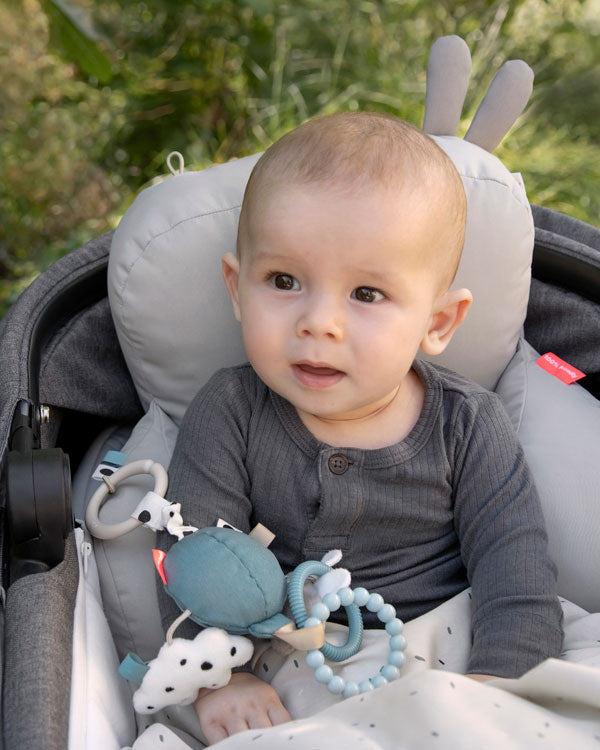 child sitting in pram with pram pillow and activity toy