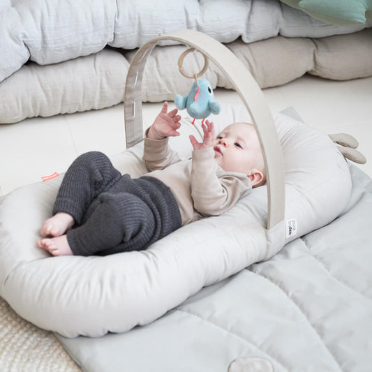 baby lying in the Done by Deer baby cosy lounger playing with a toy bird